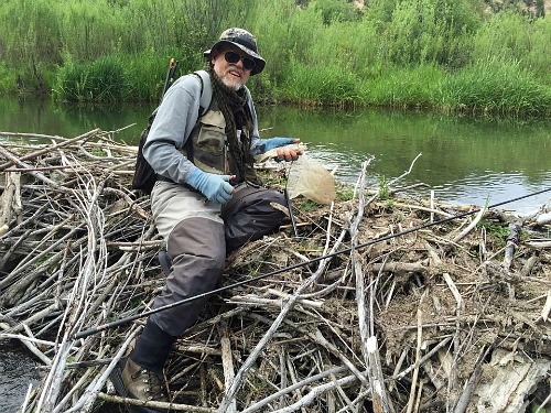 Angler sitting on beaver dam holding a fish