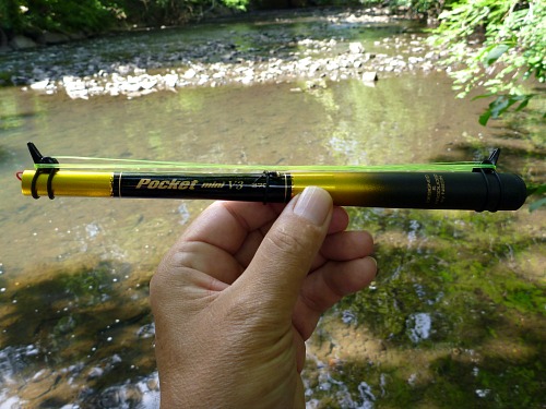 Angler holding collapsed Pocket Mini, with stream in background