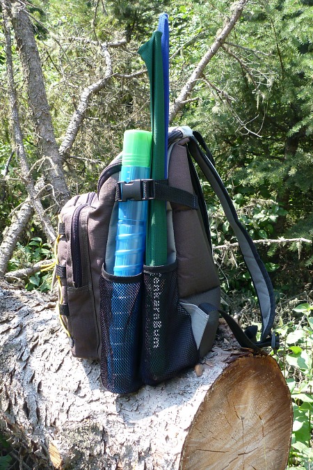 Backpack sitting on a log, showing rod and rod case in side pocket