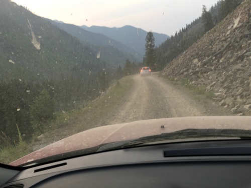 View through the windshield of a narrow, dirt road. No shoulder and steep drop.